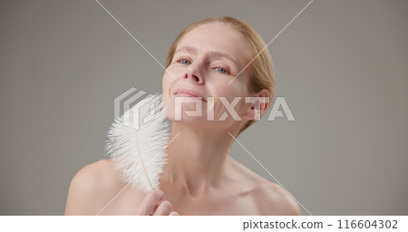Real people - concept of age, beauty, health and dry skin care - beautiful mature Caucasian middle-aged woman in her 50s holds a white fluffy feather as a symbol of lightness and tenderness Real people - concept of age, beauty, health and dry skin care - beautiful mature Caucasian middle-aged woman in her 50s holds a white fluffy feather as a symbol of lightness and tenderness 116604302