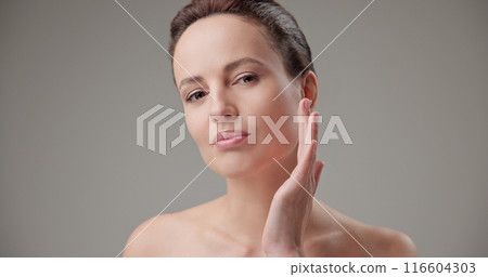 Beauty, health, cosmetics, anti-aging therapy and skin care concept - young beautiful brunette Caucasian woman touching face and looking at camera Beauty, health, cosmetics, anti-aging therapy and skin care concept - young beautiful brunette Caucasian woman touching face and looking at camera 116604303