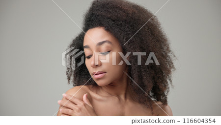 Beauty and healthcare concept - beautiful African American woman with curly afro hairstyle and clean, healthy skin touches her cheek and face with her hand, posing and looking at the camera 116604354