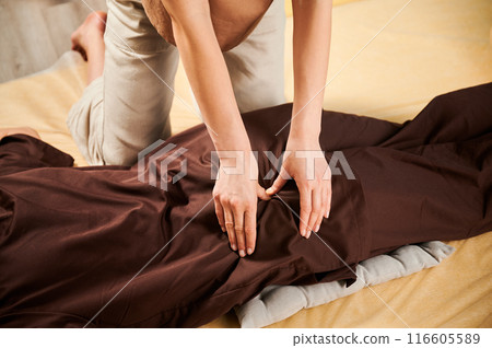 Masseuse making thai yoga massage. Cropped view of woman therapist doing traditional massage treatment for female patient indoors. Client lying on mat, meditating, enjoying hand massage. 116605589