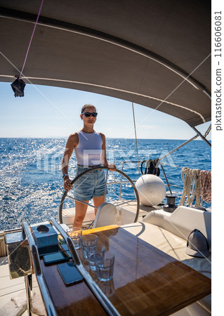Young woman female captain stands at the helm and controls a sailboat during a journey by sea 116606081