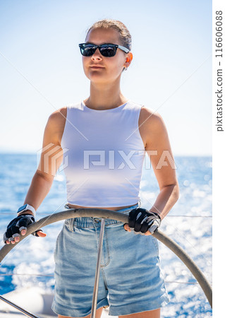 Young woman female captain stands at the helm and controls a sailboat during a journey by sea 116606088