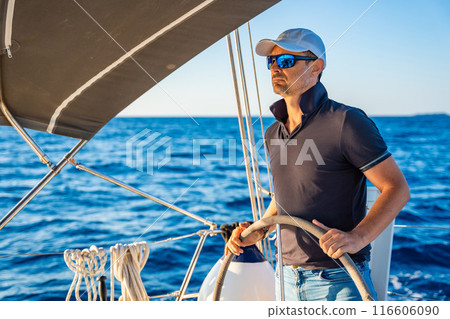 Young man captain stands at the helm and controls a sailboat during a journey by sea 116606090