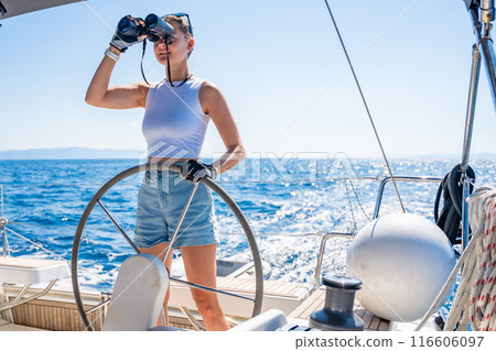 Young female captain on the yacht looking through binoculars during sailing boat control. Travel and active life. Yachting 116606097