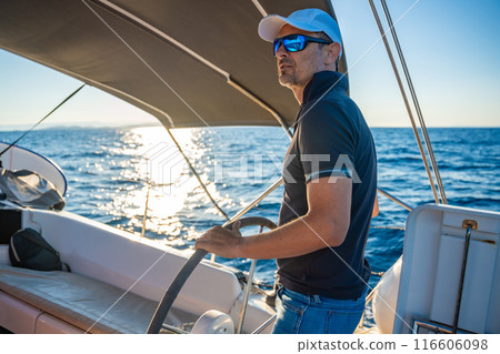 Young man captain stands at the helm and controls a sailboat during a journey by sea Young man captain stands at the helm and controls a sailboat during a journey by sea 116606098