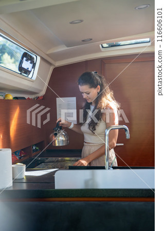 Young woman standing and preparing tea in kitchen in cabin of modern yacht during sailing in sea. Yacht life concept 116606101