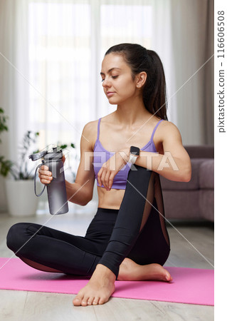 athletic fitness woman drinking water sitting on pink exercise mat at home 116606508
