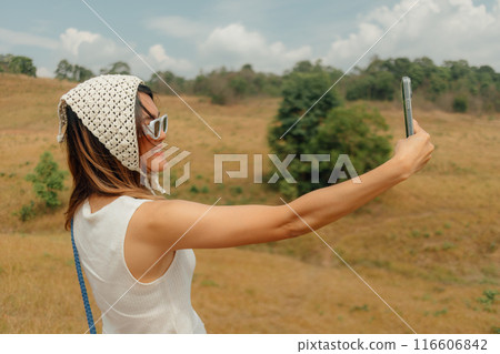 Woman taking photo of scenic hills and selfie with mobile phone. 116606842