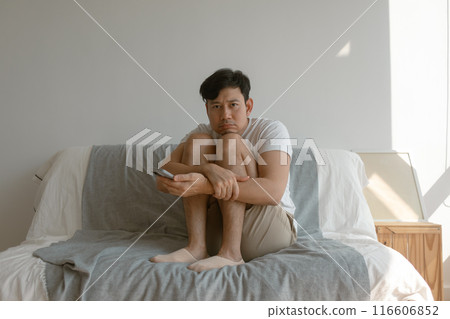 Man is hugging his knees sits on the sofa and using mobile phone. 116606852