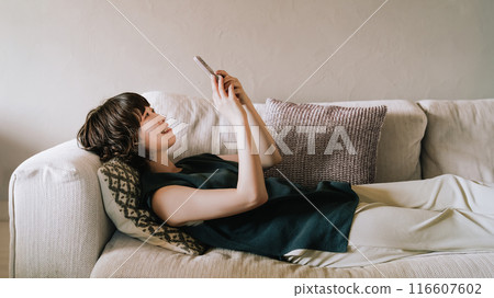 A smiling Japanese woman lying on the sofa and using a smartphone 116607602