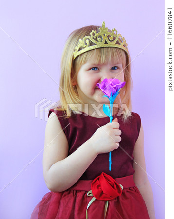 Little girl dressed as princess with crown smelling artificial flower 116607841