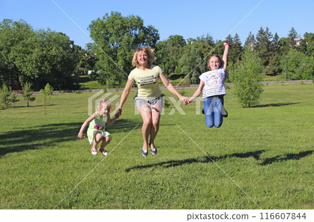 Happy mother having fun jumping with her daughters on green grass Happy mother having fun jumping with her daughters on green grass 116607844