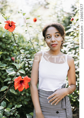 Young Woman in Garden with Red Hibiscus Flowers Enjoying Nature on a Sunny Day 116607877