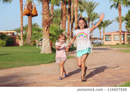 Happy sisters run on footpath in tropical resort. Sisters relaxing on vacations 116607886