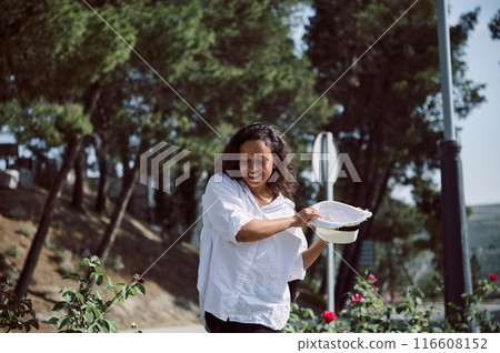 Smiling woman in white shirt with hat enjoying a sunny day outdoors in a park 116608152