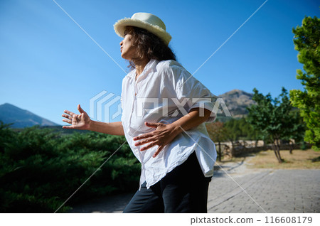 Woman in white shirt and hat enjoying nature with mountain in background Woman in white shirt and hat enjoying nature with mountain in background 116608179