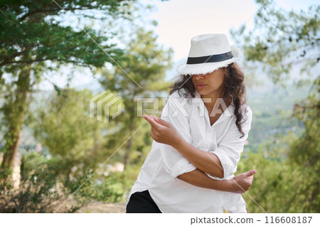 Confident woman in white hat dancing in a natural outdoor setting 116608187