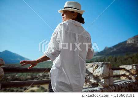 Woman in white hat and shirt enjoys scenic mountain view on a sunny day 116608191