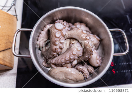 From above of whole raw octopus boiling in pot on modern black induction cooker 116608871