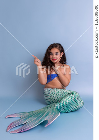 A happy girl in a mermaid costume sits on a blue background 116609000