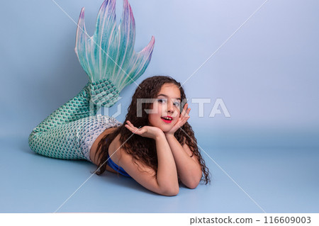 Adorable child girl in a mermaid costume lie isolated on light-blue background 116609003