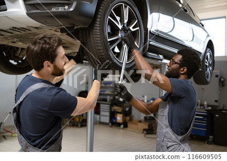 Two mechanics working on car wheel in auto repair shop 116609505