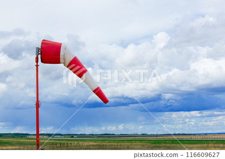 Weather vane in the airfield with grass and dramatic cloudy sky. 116609627