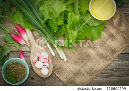Fresh ripe vegetables on the wooden table with burlap table cloth - raddish sliced on a big spoon and whole, green onion, lettuce, dried herbs in a little prep bowl with basil leaves and olive oil are Fresh ripe vegetables on the wooden table with burlap table cloth - raddish sliced on a big spoon and whole, green onion, lettuce, dried herbs in a little prep bowl with basil leaves and olive oil are 116609899