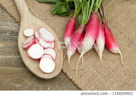 Fresh and clean red and white radish (French breakfast variety), slices on the rustic big spoon are on the burlap cloth on the wooden table. 116609903
