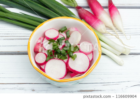 Salad of sliced radishes (French breakfast variety) and green onions in a little bowl with ingredients on the white wooden rustic table. 116609904