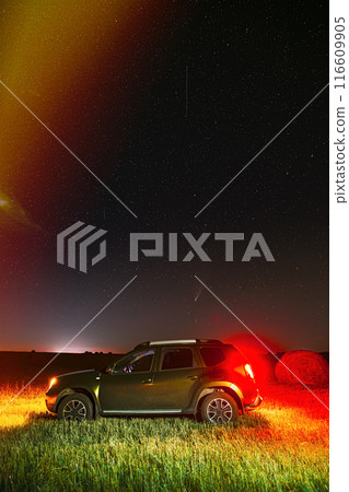 Galaxy In Night Starry Sky With Glowing Stars Above Green Car SUV In Countryside Landscape. Starry night sky And Rural Field Meadow. Comet Neowise C2020 F3 In Night Starry Sky Above Car Suv In Summer 116609905