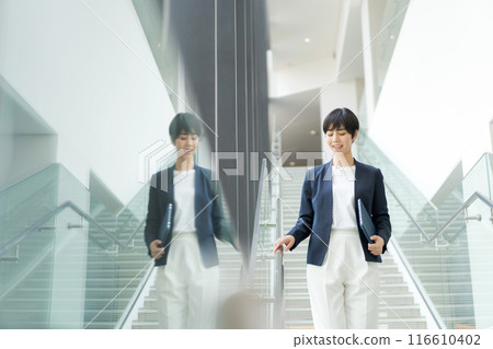 A woman in a suit walking down an office corridor 116610402