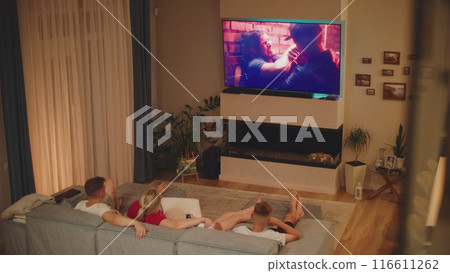 Caucasian family lying on sofa in living room and watching action movie on TV 116611262