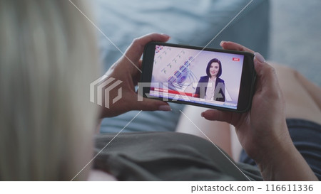 Woman watching TV news broadcast about elections in the United States using smartphone Woman watching TV news broadcast about elections in the United States using smartphone 116611336