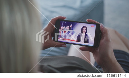 Woman watching TV news broadcast about elections in the United States using smartphone 116611344