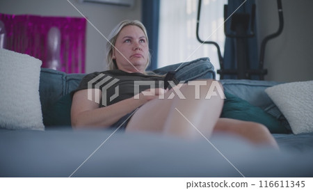 Caucasian woman watches television or movie, uses remote control Caucasian woman watches television or movie, uses remote control 116611345