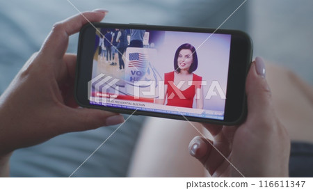 Close up of woman watching news about elections in the United States using smartphone 116611347