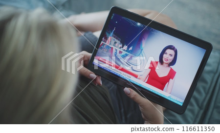 Woman watches breaking news about US election using tablet lying on sofa 116611350
