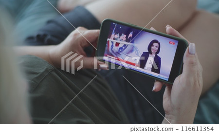 Woman watching TV news broadcast about elections in the United States using smartphone 116611354