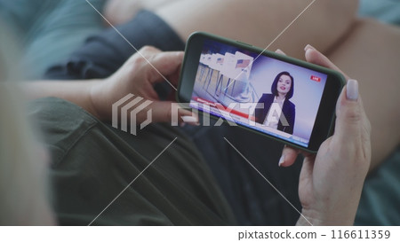Woman watching TV news broadcast about elections in the United States using smartphone 116611359