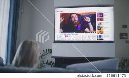Woman watches video about stock trading on the big TV screen sitting on sofa 116611473