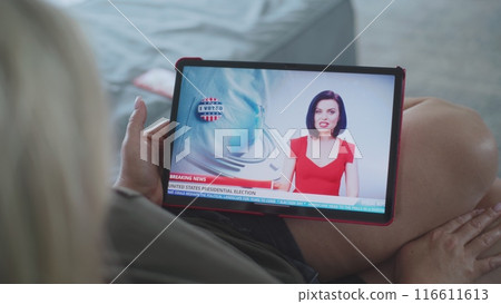 Woman watches breaking news about US election using tablet lying on sofa 116611613