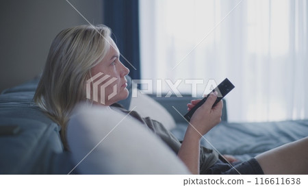 Adult woman watches television, uses remote control for TV 116611638
