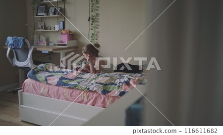 Young girl lies on cozy bed and uses digital tablet computer 116611682