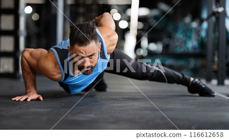 Strength exercise. Muscular man doing push ups on on hands in gym, panorama 116612658