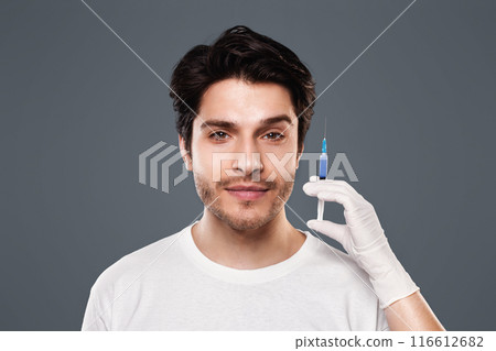 Beautician hands holding syringe with transparent liquid near male face, aesthetic cosmetology and beauty care Beautician hands holding syringe with transparent liquid near male face, aesthetic cosmetology and beauty care 116612682