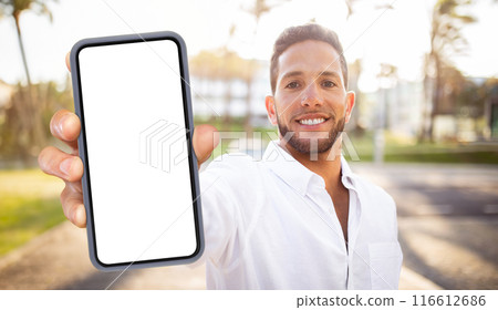 A smiling man in a white shirt holds a smartphone with a blank screen in front of him. The phone is in focus, while the man is blurred in the background. A smiling man in a white shirt holds a smartphone with a blank screen in front of him. The phone is in focus, while the man is blurred in the background. 116612686