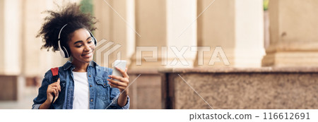 Educational Podcast. African American Student Girl Using Phone Wearing Wireless Headphones Walking At University Campus Outdoor. People And Gadgets, E-Learning Application Concept, Copy Space 116612691