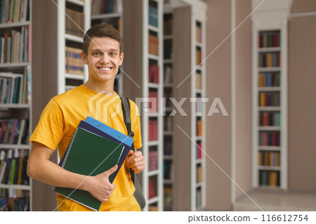 Knowledge. Excited caucasian male student posing next to bookshelves in campus library, empty space Knowledge. Excited caucasian male student posing next to bookshelves in campus library, empty space 116612754
