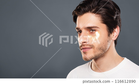 Young man with golden patches under eyes from wrinkles and dark circles, grey studio background Young man with golden patches under eyes from wrinkles and dark circles, grey studio background 116612890